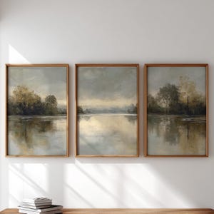 Könnte beinhalten: Drei gerahmte Landschaftskunst-Drucke. Jeder Druck zeigt eine ruhige Seeszene mit Bäumen und einem bewölkten Himmel. Das Kunstwerk ist in gedämpften Tönen von Grau, Beige und Braun gehalten, mit Holzrahmen.