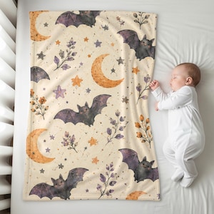 May include: A rectangular blanket featuring a cream-colored background with a repeating pattern of dark purple bats, orange crescent moons, small stars, and sprigs of purple and orange leaves. The design is printed across the entire fabric surface.