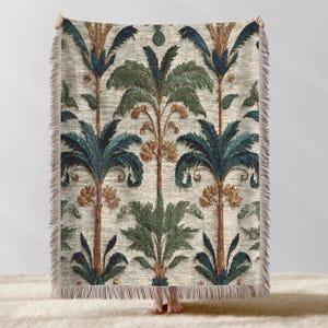 Puede incluir: Una manta beige con un patrón repetido de palmeras estilizadas en tonos azules, verdes y marrones. La manta tiene un borde con flecos. El diseño recuerda a las ilustraciones botánicas vintage.