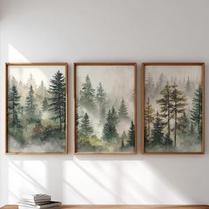 以下が含まれることがあります： 霧のかかった森の風景を描いた、3つの額装された水彩画プリント。このアートワークは、緑と茶色の色合いの背の高い常緑樹と、柔らかく雰囲気のある霧が特徴です。フレームは明るい茶色の木材で作られています。