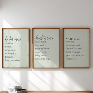 Könnte beinhalten: Drei gerahmte Kunstdrucke mit Holzrahmen. Die Drucke zeigen inspirierenden Text auf hellgrünem Hintergrund. Der Text enthält Sätze wie "durch sein Kreuz", "Christus ist auferstanden" und "neu gemacht". Die Rahmen sind rechteckig.