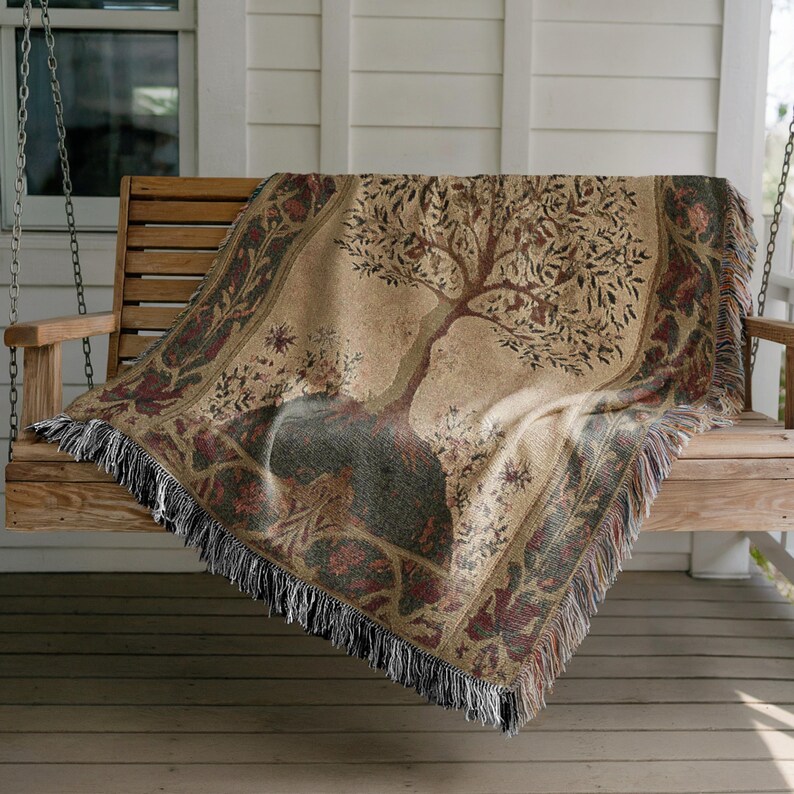 Peut inclure: Une couverture beige avec un motif d'arbre drap&eacute;e sur une balan&ccedil;oire en bois. L'arbre a des branches marron et des feuilles vertes. La couverture a une bordure d&eacute;corative avec des franges.