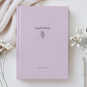 Puede incluir: Un diario de tapa dura de color lavanda con las palabras "chapter thirty" y una ilustración de pastel. El nombre del autor, "TONYA CLEMMINGS", está impreso en la parte inferior. El diario está sobre una superficie blanca.