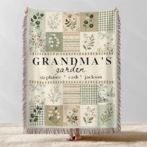 May include: A cream-colored throw blanket with a patchwork design featuring floral patterns and green squares. The text "GRANDMA'S garden" is displayed in the center, with names below. The blanket has a fringed edge.