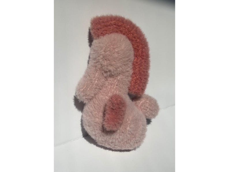 Op de afbeelding: Een pluche speelgoed in roze en roze tinten. Het speelgoed heeft een afgerond lichaam met een donkerroze accent op de rug en een roze mohawk-stijl detail bovenop. Het speelgoed is zacht en pluizig.
