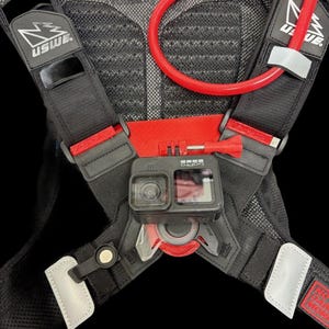 Op de afbeelding: Zwarte hydratatie rugzak met rode accenten en een zwarte GoPro camera gemonteerd aan de voorkant. De rugzak heeft een mesh rugpaneel en verstelbare banden. De hydratatie rugzak heeft een rode hydratatieslang met een bijtklep.