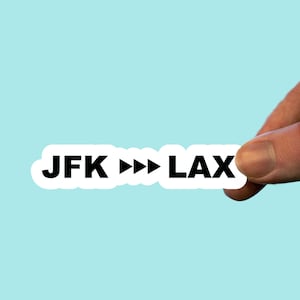 May include: White sticker with black text that reads "JFK >>> LAX".