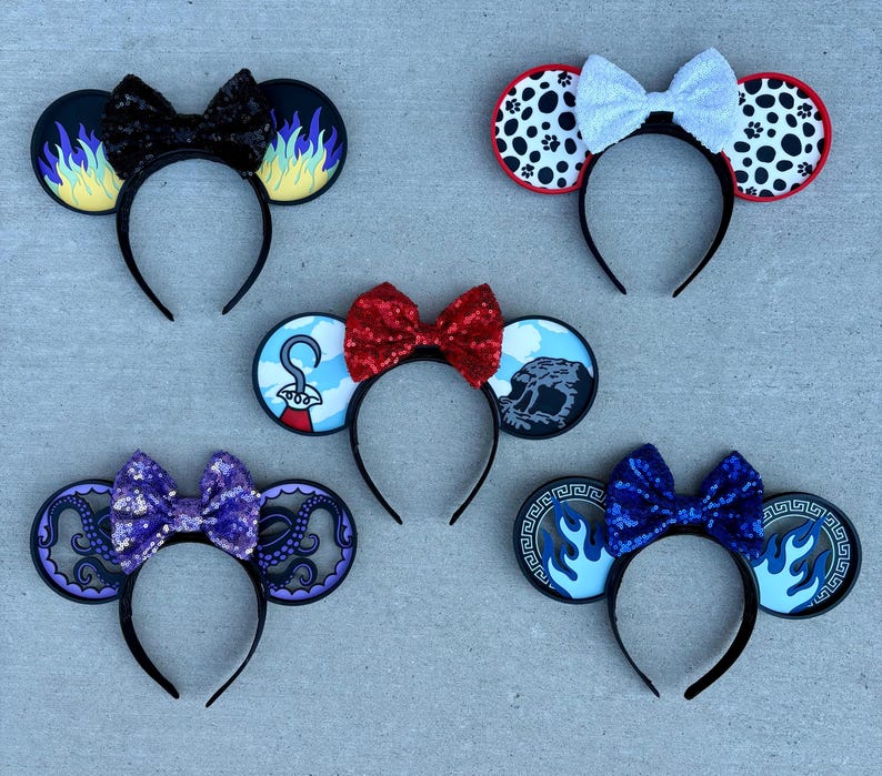 May include: Five decorative headbands with mouse ears. Each headband features a different design, including flames, Dalmatian spots, a pirate hook, an octopus, and flames. The headbands have bows in various colors, including black, white, red, purple, and blue.