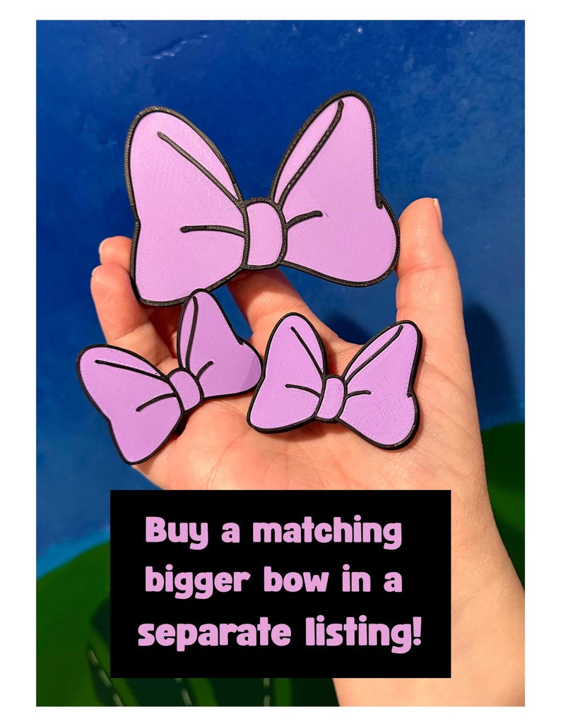 May include: Three lavender-colored bow-shaped accessories with black outlines. The bows are in different sizes. Text on a black background reads: "Buy a matching bigger bow in a separate listing!"