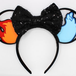 May include: Black headband with a black sequined bow and two ears. One ear is orange and red and shaped like a flame. The other ear is blue and shaped like a wave.