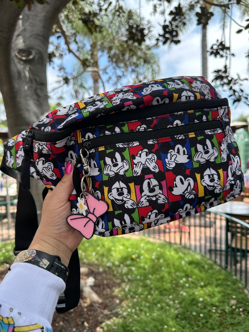 May include: Black fanny pack with a colorful print of Mickey Mouse doing the "See No Evil, Hear No Evil, Speak No Evil" pose. The fanny pack has two zippered compartments and a black strap.