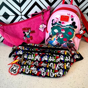 May include: Three pink and black Disney-themed bags. The largest bag is a pink backpack with a red zipper and a white Alice in Wonderland design. The middle bag is a pink corduroy shoulder bag with a Mickey Mouse design. The smallest bag is a black fanny pack with a colorful Mickey Mouse design.