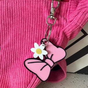 May include: A pink corduroy bag with a silver zipper and a pink and white bow keychain with a white flower charm.