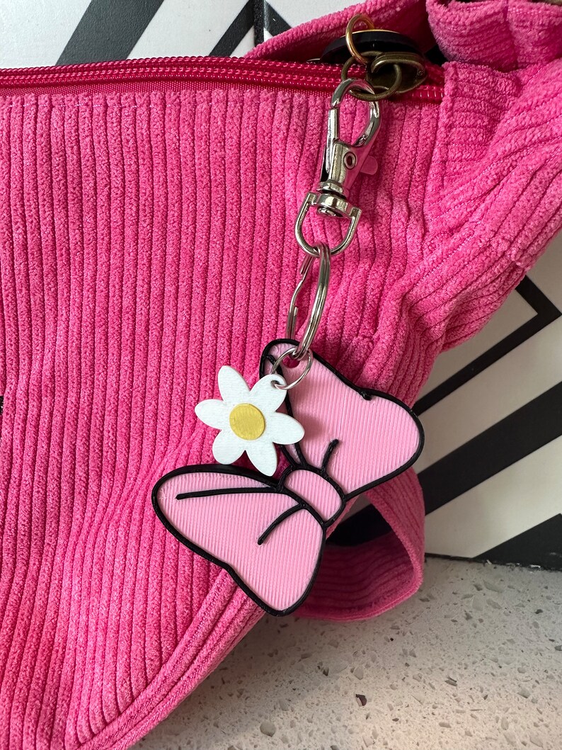 May include: A pink corduroy bag with a silver zipper and a pink and white bow keychain with a white flower charm.