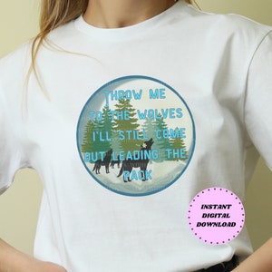 Może przedstawiać: Biała koszulka z niebieskim kołem graficznym przedstawiającym zimową scenę z wilkami i tekstem "THROW ME TO THE WOLVES I'LL STILL COME OUT LEADING THE PACK".