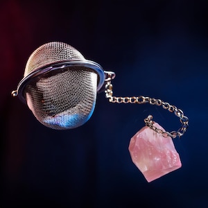 May include: A silver tea infuser with a chain and a pink crystal attached to the end of the chain.