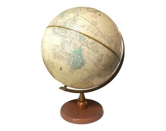 May include: A vintage-style globe with a cream-colored surface, displaying detailed geographical features. The globe is supported by a brass meridian ring and a wooden base. The globe is a decorative item.