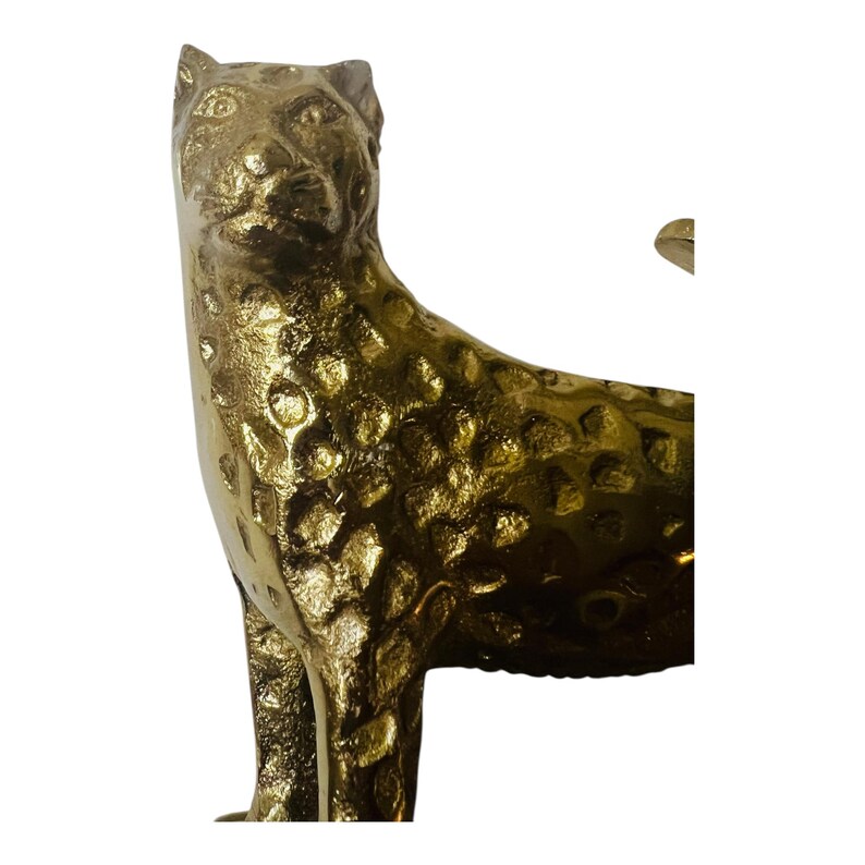 May include: A gold-colored leopard statue with a textured surface. The sculpture depicts the animal in a standing pose, with its head turned slightly. The leopard's spots are visible on its body.