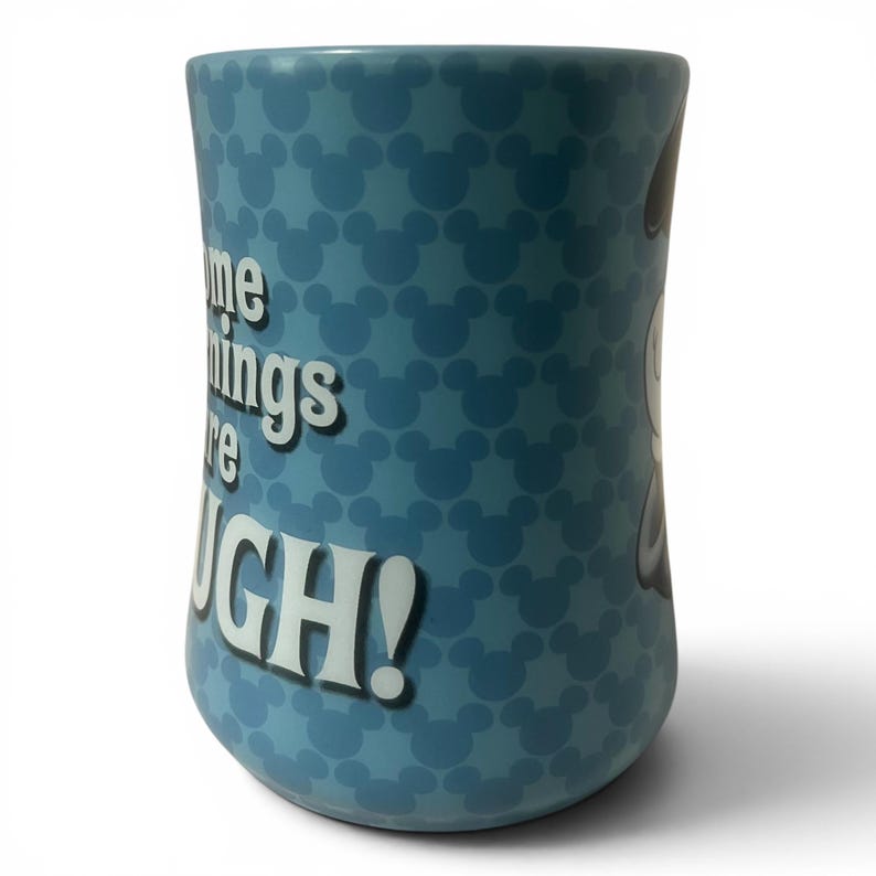 May include: A blue ceramic mug with a pattern of Mickey Mouse silhouettes. The mug has the text "Some things are tough!" in white. The mug is cylindrical and has a white background.