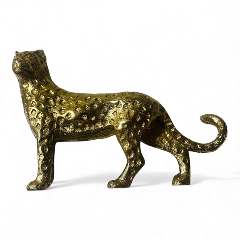 May include: A golden leopard figurine with a textured surface and spotted pattern. The sculpture is posed in a standing position with its tail curled upwards. The figurine is made of metal and has a shiny finish.