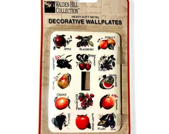 May include: Decorative wallplate featuring a variety of colorful fruit illustrations, including apples, blackberries, and plums. The wallplate is made of heavy-duty metal and has a rectangular shape with a single switch opening. The text "WALDEN HILL COLLECTION" is visible.