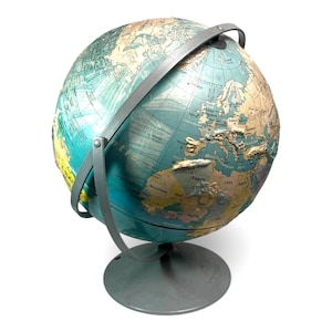 May include: A vintage globe with a teal and tan color scheme, featuring a detailed map of the world. The globe is supported by a gray metal stand and has a gray metal meridian. The continents are depicted in shades of tan and brown, with oceans in teal.