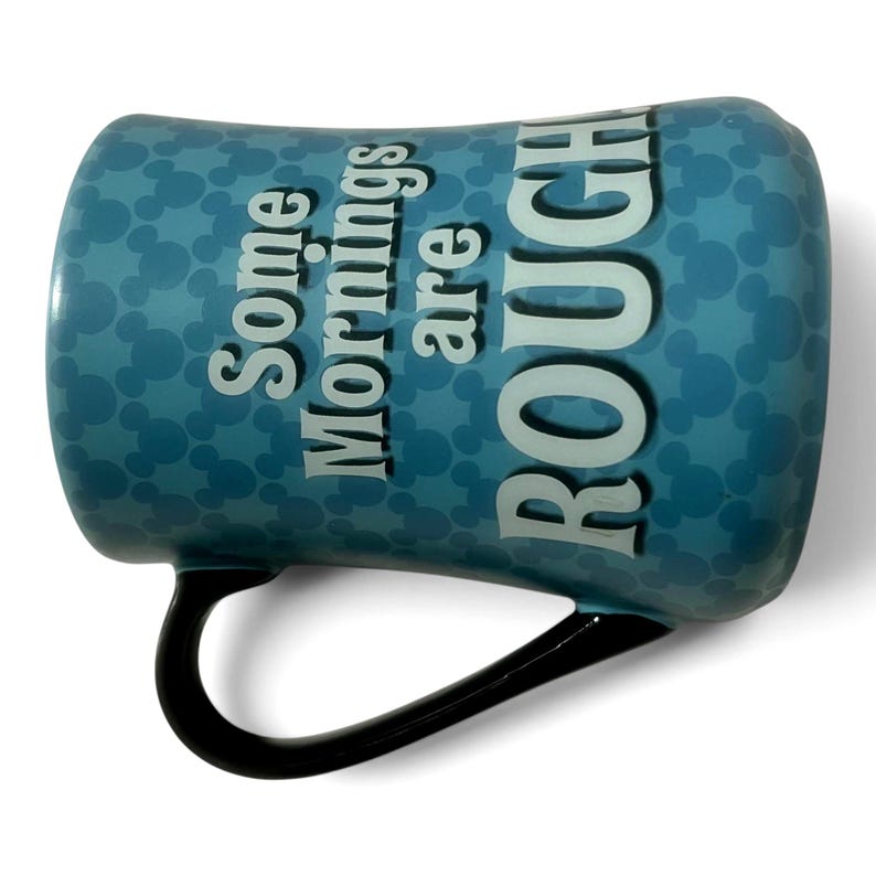 May include: A blue ceramic mug with a black handle. The mug features a pattern of small circles and the text "Some Mornings are ROUGH" in white. The mug is designed for hot beverages.