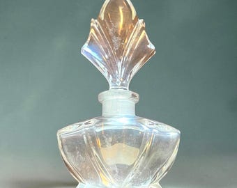 May include: A clear glass perfume bottle with an iridescent finish and a wide, faceted base. The bottle features a tall, pointed, leaf-shaped stopper that fits into a ribbed neck, creating a decorative vessel with reflective surfaces.