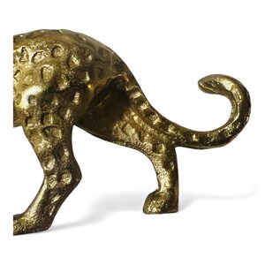 May include: A golden, textured metal sculpture of a cheetah, showcasing its hindquarters and curled tail. The sculpture has a hammered appearance, with visible spots and a polished finish. The cheetah's legs are firmly planted, suggesting a poised stance.