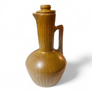 May include: A brown ceramic pitcher with a lid and a handle. The pitcher has a textured surface and a ribbed design.