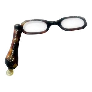May include: A pair of brown and black reading glasses with a decorative handle. The handle is embellished with rhinestones. The glasses have a small, round, clear foot at the bottom of the handle.