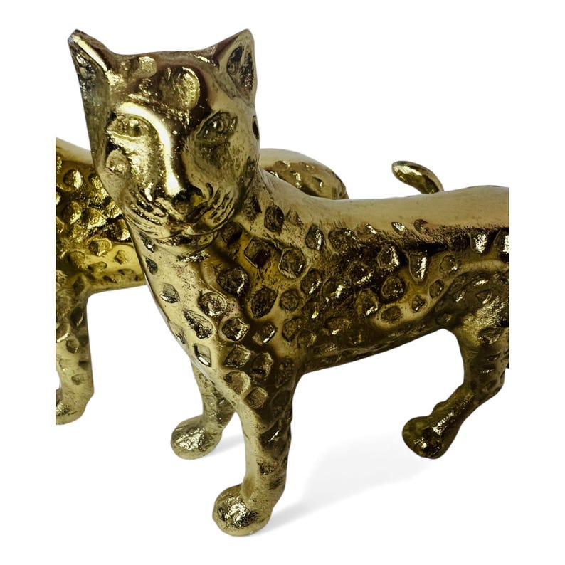 May include: Two gold-colored leopard figurines. The figurines have a textured surface with spots and are posed in a walking stance. The details include the leopard's head, ears, and tail. The background is white.