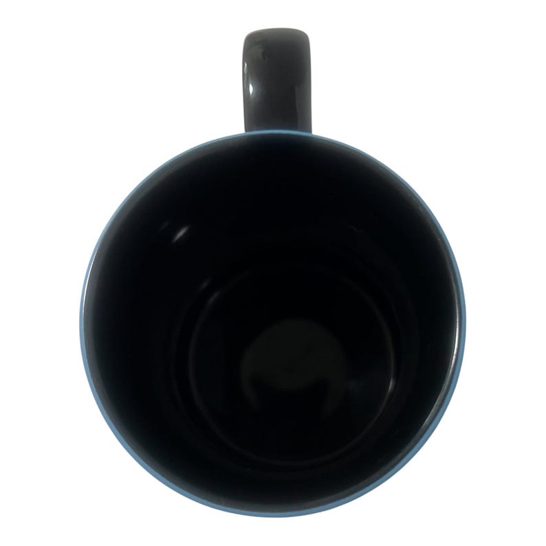 May include: A black ceramic mug with a dark gray handle and a light blue rim. The interior of the mug is black. The mug is viewed from above against a white background.