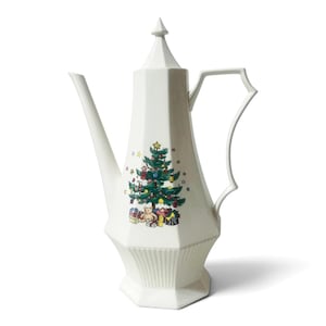 May include: A tall, off-white ceramic coffee pot with a faceted, hexagonal body and a pointed lid. The front features a colorful illustration of a decorated Christmas tree with ornaments, a star topper, and wrapped gifts at the base.