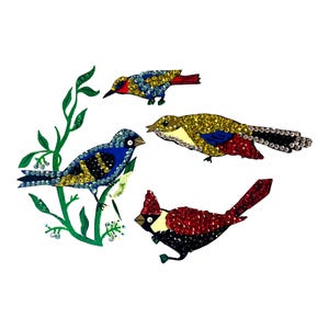 May include: Four bejeweled bird designs in various colors, including blue, red, yellow, and black, are arranged on a white background. One bird is perched on a green leafy branch. The birds are embellished with sparkling sequins.