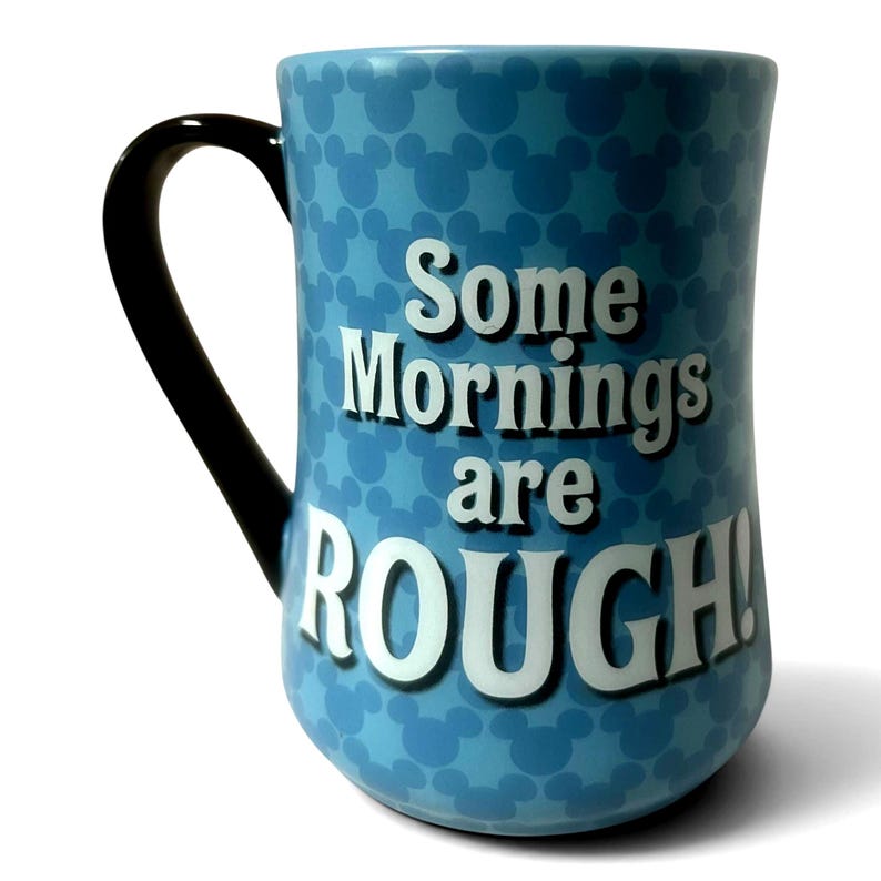 May include: A light blue ceramic mug with a black handle. The mug features a pattern of Mickey Mouse silhouettes and the text "Some Mornings are ROUGH!" in white block letters.
