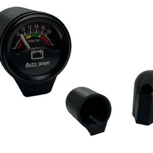 May include: Black Auto Gage voltmeter with a curved needle and a battery symbol. The gauge displays voltage readings from 8 to 18 volts. Includes two black plastic caps.