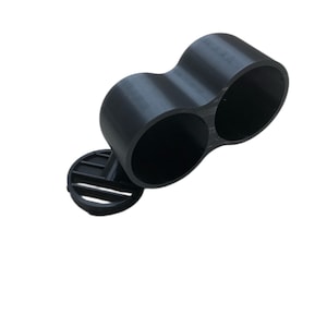 May include: A black plastic double-cylinder holder with a round base. The holder is designed to hold two cylindrical objects, such as pens or pencils.