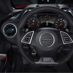 May include: Black leather-wrapped steering wheel with a silver Camaro logo and red stitching. The steering wheel has silver buttons and controls. The dashboard features a digital display with the number "0" and a speedometer that reads up to 160 mph.