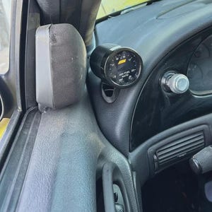 May include: A black circular AEM air/fuel ratio gauge mounted on the dashboard of a vehicle interior. The gauge features a black face with white numerical markings ranging from 9 to 20, with the text AIR/FUEL RATIO printed in white on the display.