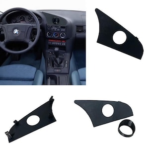 May include: Black car interior trim pieces, including a dashboard and side panel, with a circular opening. The image also shows a car's steering wheel and center console. The trim pieces appear to be replacements or accessories.