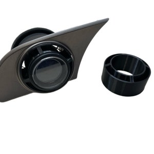 May include: A black plastic vent ring with a gray plastic vent cover. The vent cover has a circular opening with a black plastic ring around it. The vent ring is designed to fit around a car's air vent.