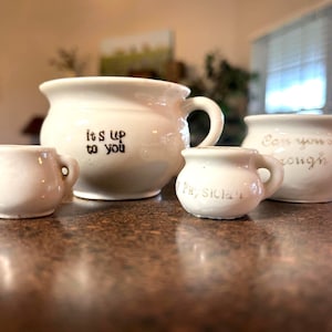 May include: Set of four white ceramic chamber pots with gold lettering. The largest pot reads "It's up to you". The next largest pot reads "Can you go long enough". The smallest pot reads "Pray, Sicken".