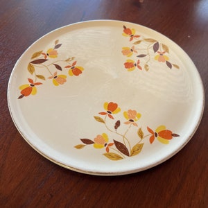 May include: A white ceramic plate with a gold rim and a floral design featuring orange, yellow, and brown flowers.
