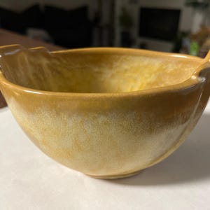 May include: A yellow ceramic bowl with a unique, wavy rim. The bowl has a speckled glaze with a light yellow and white pattern.
