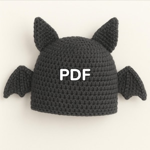 Può includere: Un cappello all'uncinetto grigio scuro a forma di pipistrello, con orecchie a punta e ali. La parola "PDF" è stampata in bianco sul davanti. Il cappello è progettato con un punto strutturato, che gli conferisce un aspetto fatto a mano.