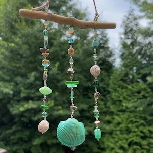 Peut inclure: Un carillon de vent en coquillage vert et blanc avec des perles et une branche de bois flotté. Le carillon de vent est suspendu à une ficelle.