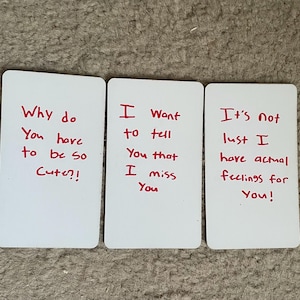 May include: Three white rectangular cards with handwritten red text. The cards read: "Why do You have to be so Cute?!", "I Want to tell You that I miss You", and "It's not lust I have actual feelings for You!"