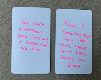 May include: Two white rectangular cards with rounded corners. The left card has the text "You Can't experience love fully with a closed mind and heart" in pink. The right card reads "There is Something from Your Past You're holding on to that's Keeping You Stuck" in pink.