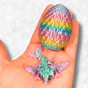 May include: A small, iridescent dragon toy hatching from a rainbow-colored egg. The dragon has pink wings, a green body, and a white face.